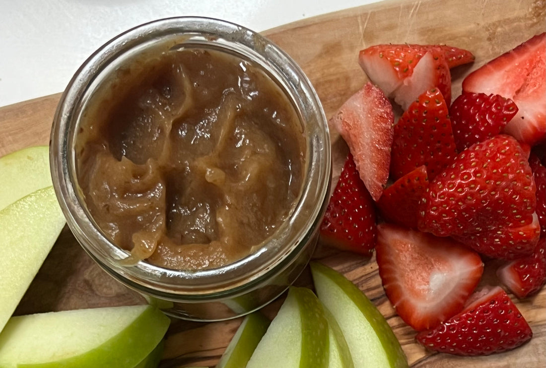 Date caramel in a small jar next to cut strawberries and apples