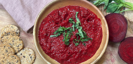 Roasted beet dip in a serving bowl with seeded crackers on the side