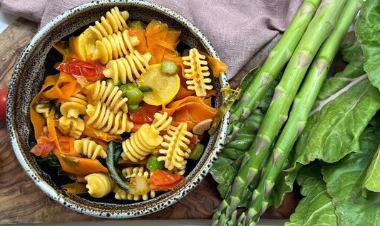 Pasta primavera in a a bowl with asparagus and rainbow chard on the side