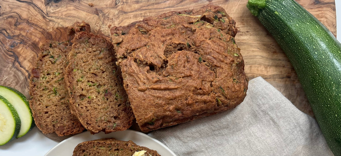 Sliced zucchini loaf on a cutting board with a zucchini and zucchini slices on the side  