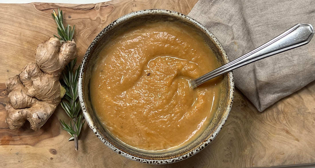 Carrot ginger soup on a cutting board with ginger and rosemary 