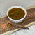 
                  small bowl of lentil soup on a cutting board with red lentils spread around and a teaspoon next to the bowl with turmeric powder in it
                
