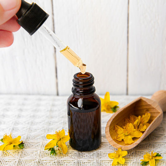 Flowers of St Johns wort near a small bottle with dropper full of st johns wort oil