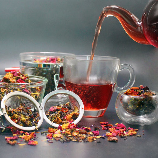 Clear cup with tea being poured into it surrounded by small bowls of raw herbs.