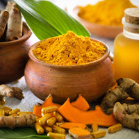 wooden bowl full of turmeric powder with cut turmeric root in front of the bowl