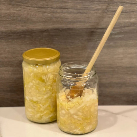 two mason jars of sauerkraut, one with a wooden spoon and the other one with a closed lid, with a wooden background