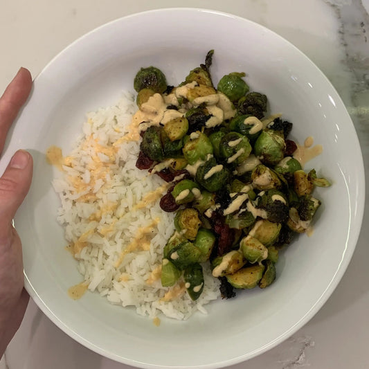 white bowl with white rice, cooked brussel sprouts and drizzle of sriracha mayo