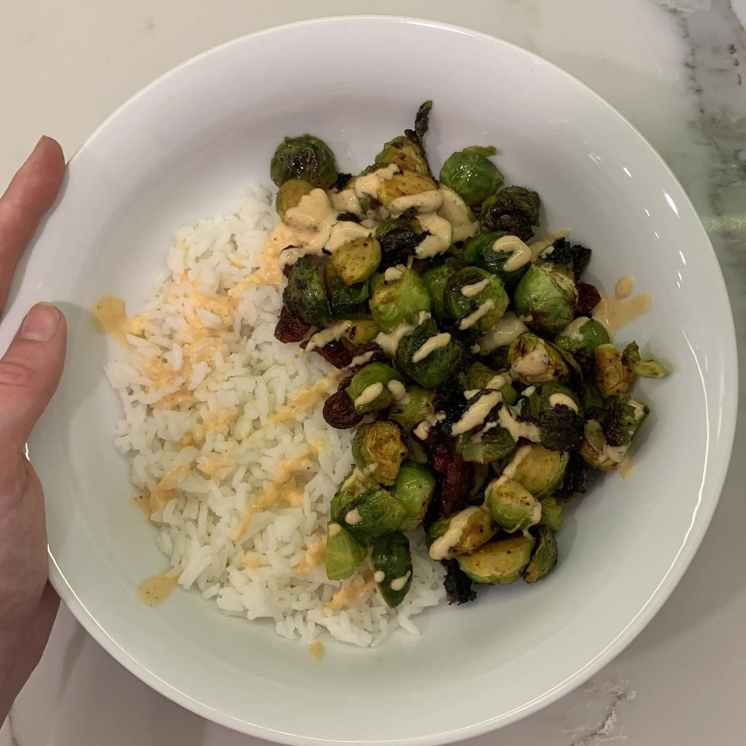 
                  white bowl with white rice, cooked brussel sprouts and drizzle of sriracha mayo
                