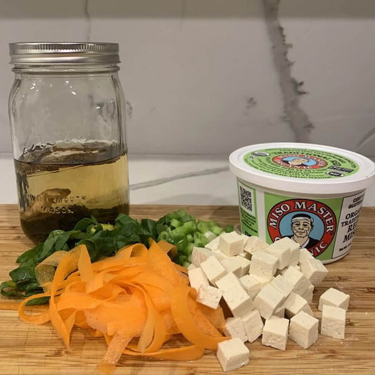Ingredients for miso soup recipe on a wooden board. Include chopped veggies, miso paste and tofu