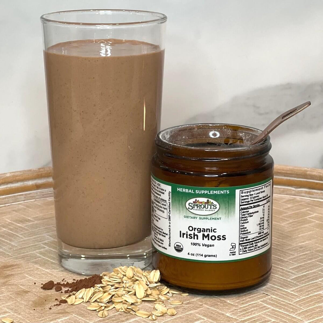 Glass of smoothie next to jar of Irish moss with rolled oats pile in front of glass