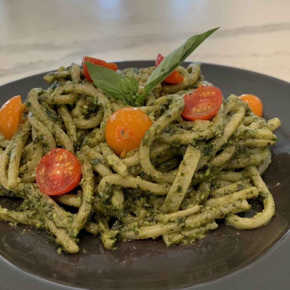plated pesto basil pasta with halved cherry tomatoes and sprig of basil.
