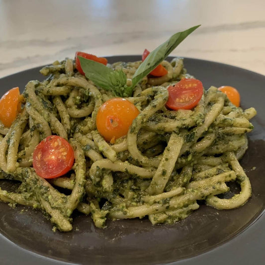 plated pesto basil pasta with halved cherry tomatoes and sprig of basil.