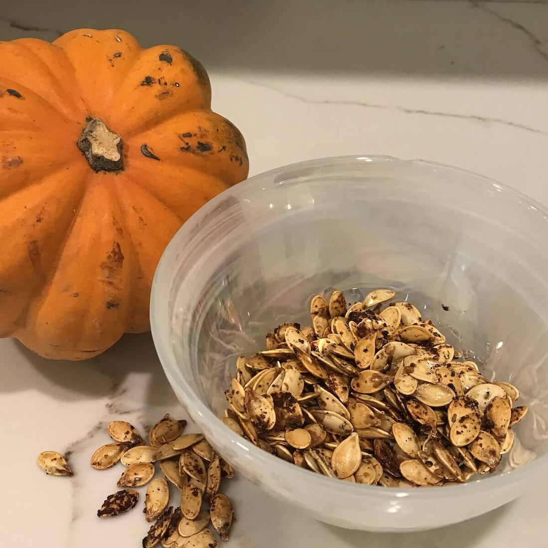 Small pumpkin next to a white bowl half filled with baked pumpkin seeds