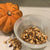 
                  Small pumpkin next to a white bowl half filled with baked pumpkin seeds
                