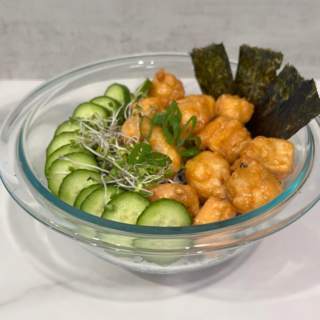 view of clear bowl with rice and black sesame seeds topped with cucumber slices. tempura sweet potato, 4 leaves of sea weed, chopped scallions and sprouts