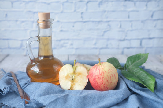 A unique bottle full of apple cider vinegar next two a half of an apple and a whole apple