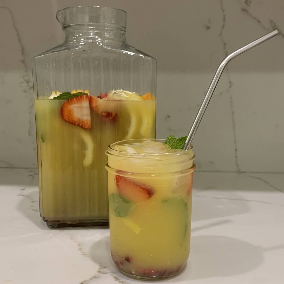 glass pitcher of mixed orange juice, yerba mate tea and fresh fruit with a mason jar filled with the juice and a metal straw