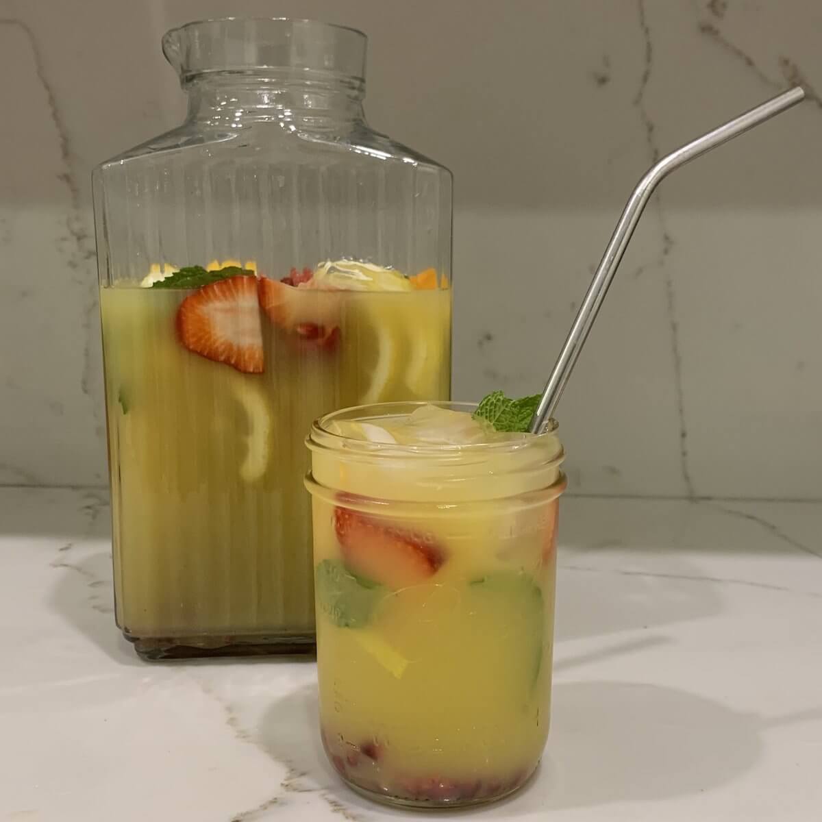 
                  glass pitcher of mixed orange juice, yerba mate tea and fresh fruit with a mason jar filled with the juice and a metal straw
                