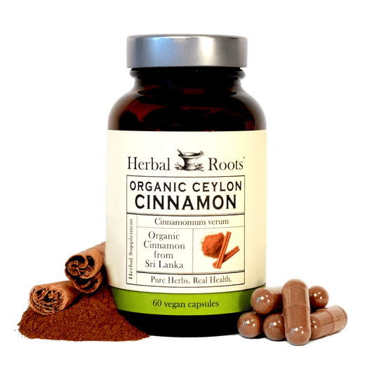 A bottle of "Herbal Roots Organic Ceylon Cinnamon" sits next to a small pile of ground cinnamon, sticks, and capsules.